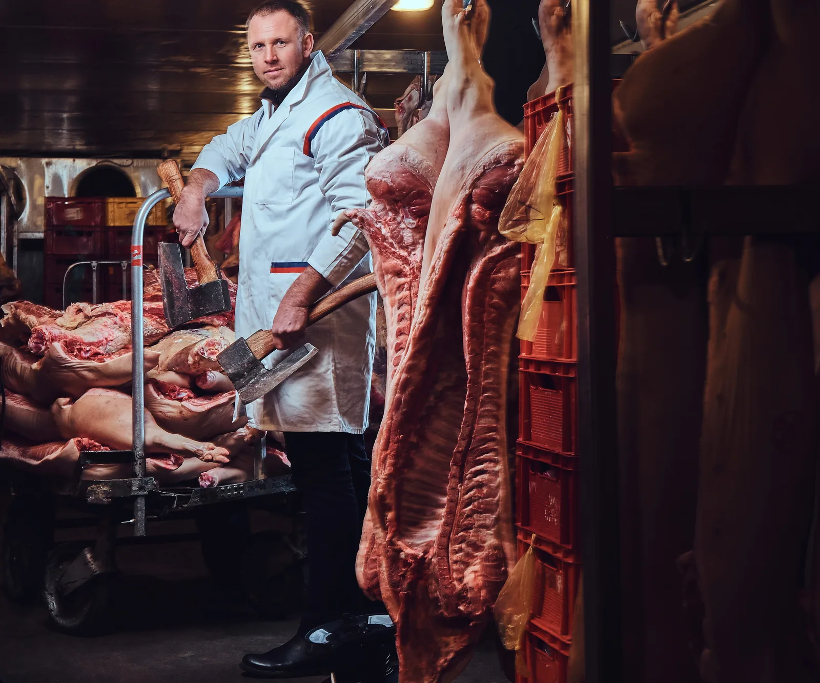 Butcher in white coat holding axes in a cold room, from Graphic House.