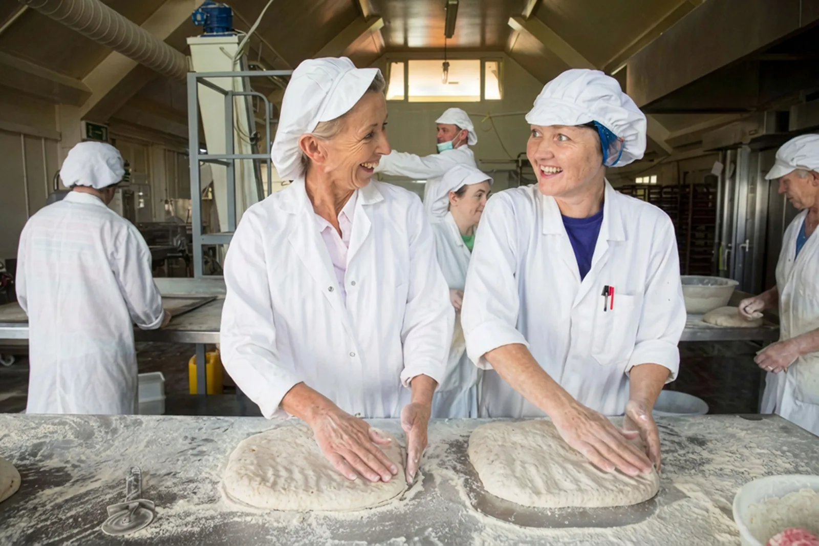 Two smiling bakers kneading dough in a commercial kitchen for website design.