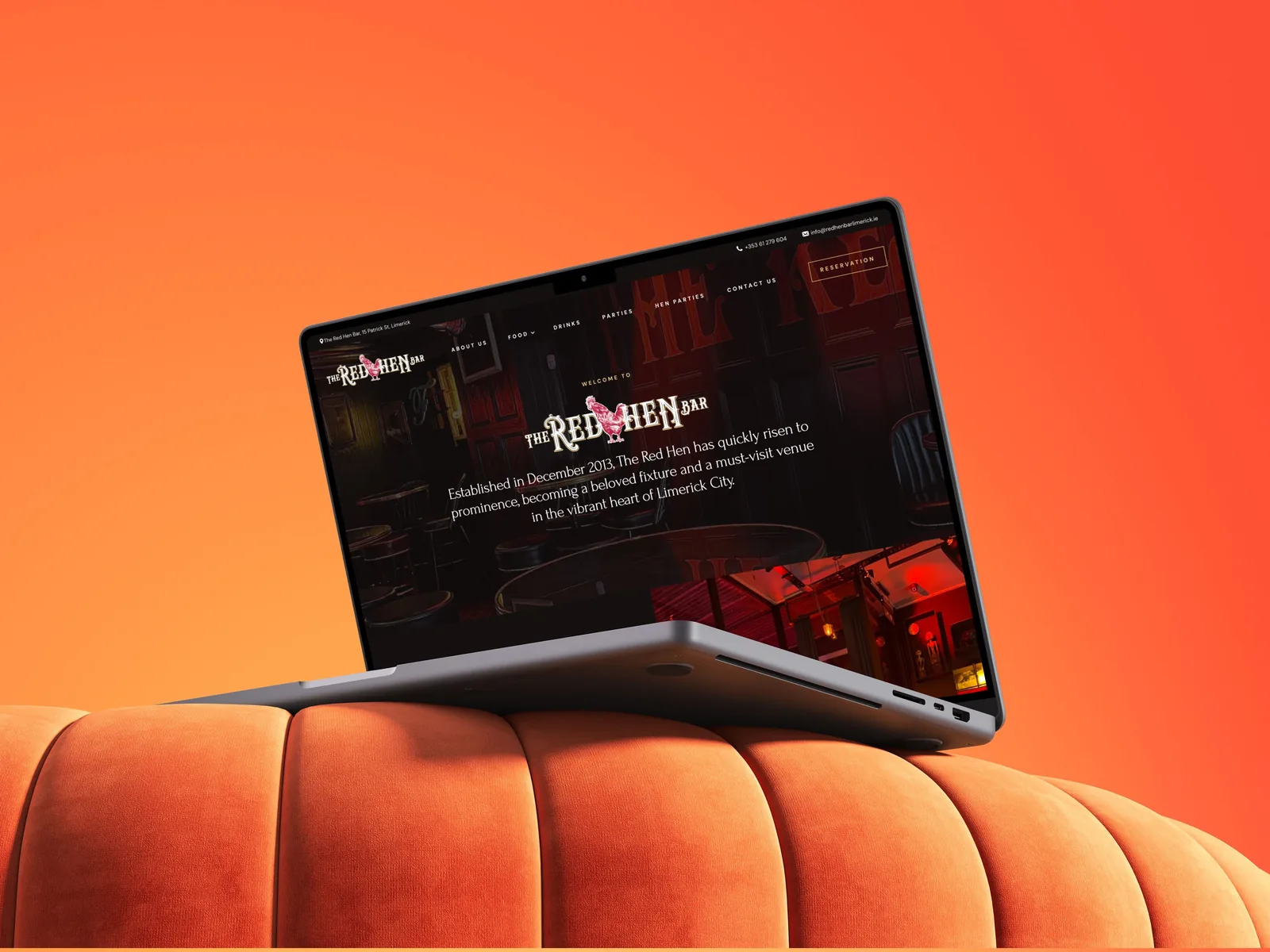 The Red Hen Bar website displayed on a laptop within a vivid orange interior